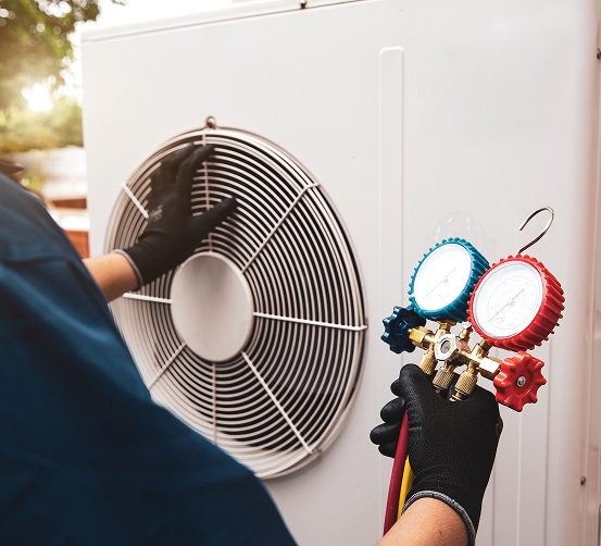 Technicien ganté vérifiant l'unité extérieure d'un climatiseur et tenant un jeu de manomètres. Maintenance CVC.