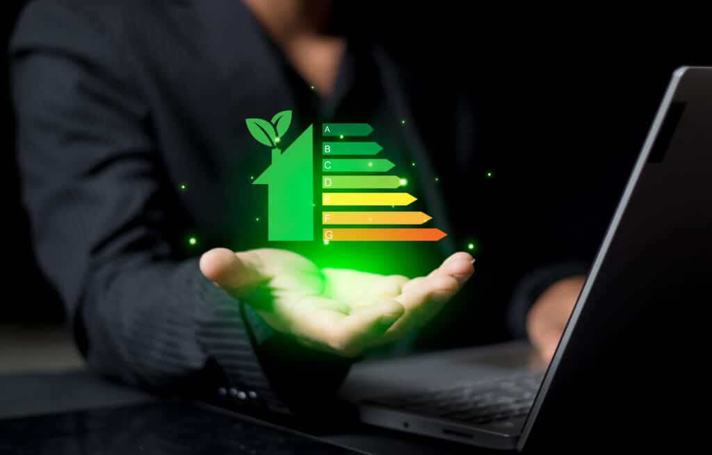 Main tenant une maison verte lumineuse avec notation énergétique A-G, symbolisant l'habitat durable et l'efficacité énergétique.