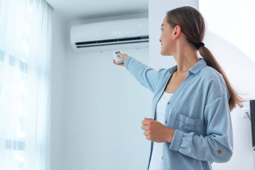 Femme ajuste la climatisation avec une télécommande murale blanche dans une pièce lumineuse pour son confort.
